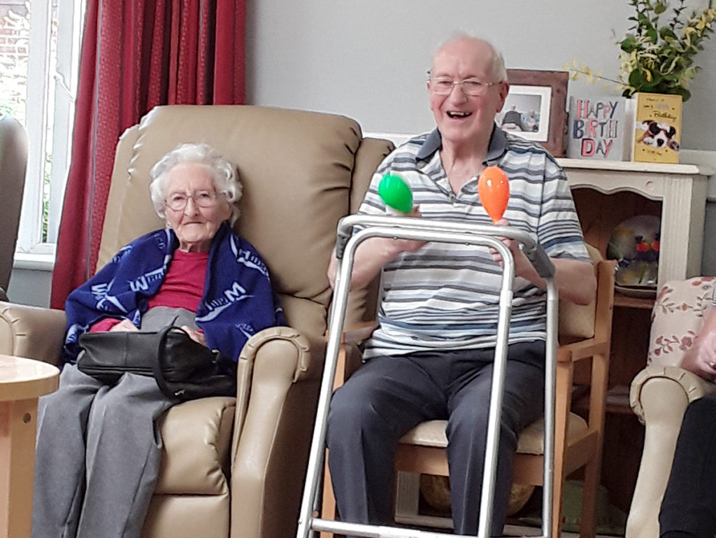 Abbotsleigh Care Home residents smiling and waving maracas to music