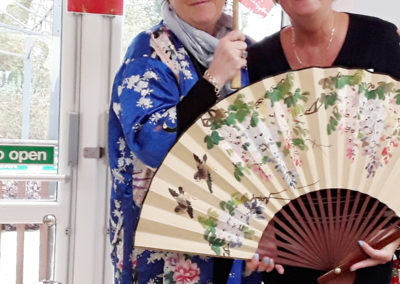 Nellsar Recreation & Welbeing Manager and a member of staff standing with a Chinese umbrella and fan at Abbotsleigh Care Home