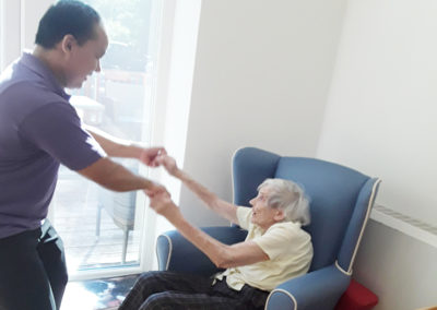 Staff member and Abbotsleigh resident holding hands while she dances in her chair