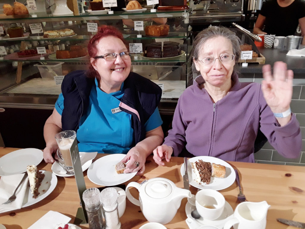 An Abbotsleigh Care Home resident and carer sat in a cafe with coffee and cake