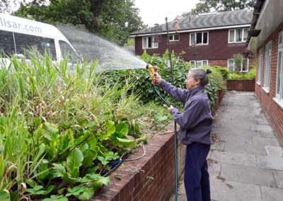 Female resident watering the plants in Abbotsleigh Care Home's front garden