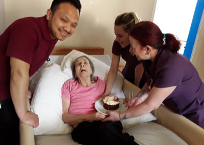Lady resident receiving a birthday cake in bed at Abbotsleigh Care Home