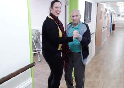 Male Abbotsleigh resident and female carer, dancing together in a corridor
