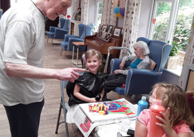 Children painting pictures at Lady resident receiving a birthday cake at Abbotsleigh Care Home