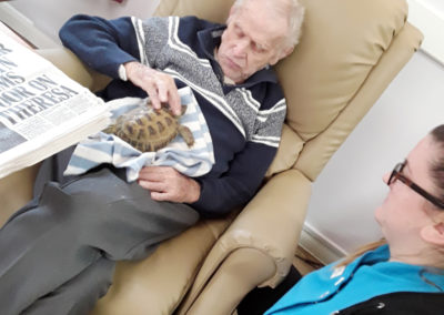 Male resident sitting with a female carer petting a tortoise on his lap