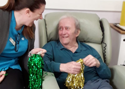 Staff and resident laughing with each other, holding glittery pom poms