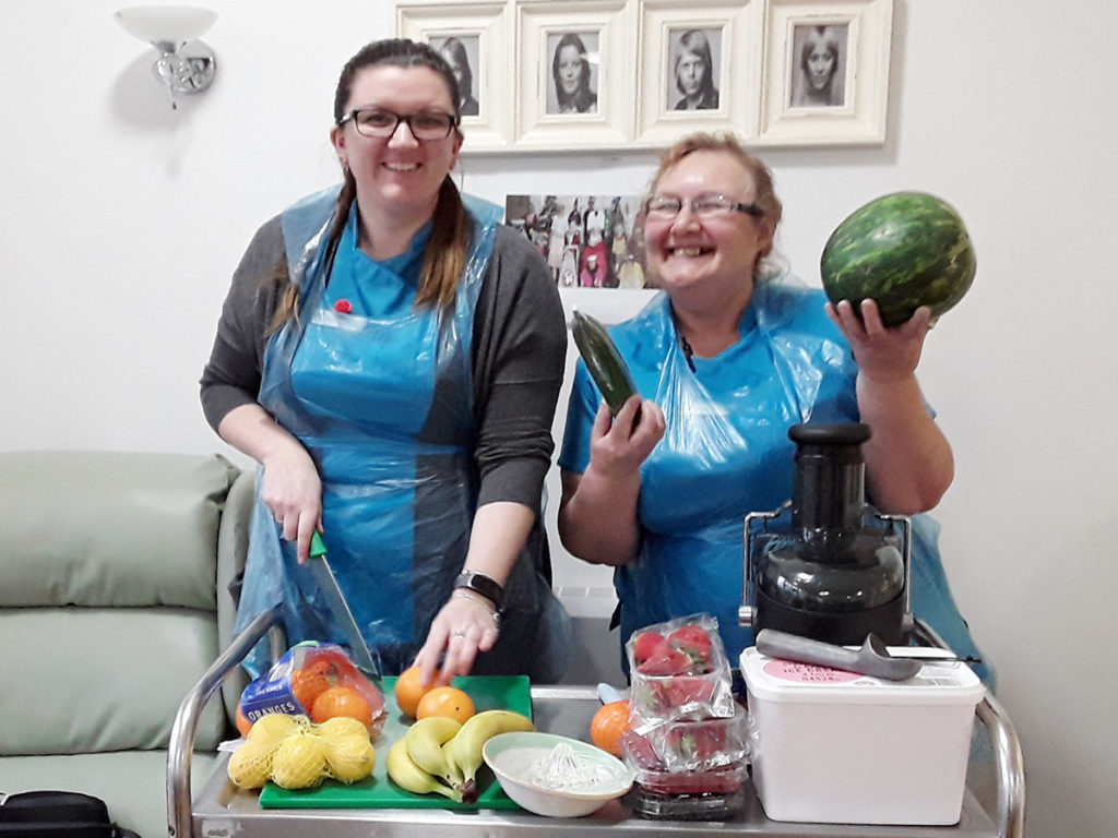 Two staff member standing at a trolley with fruit ready to go into a blender