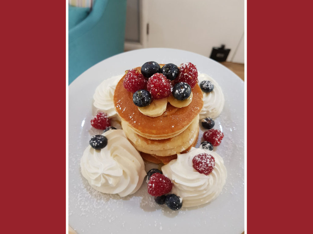 A stack of pancakes, decorated with cream and fruit