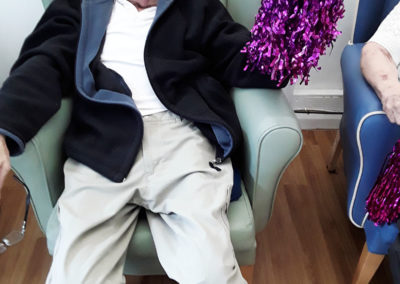 Seated lady resident, smiling with some purple glittery pom-poms