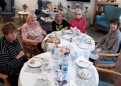 Staff and residents sat around a table enjoying afternoon tea