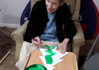 A lady resident painting a Christmas tree decoration with green paint at Abbotsleigh Care Home