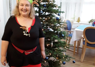 Staff member dressed as an elf, standing by a Christmas tree at Abbotsleigh Care Home